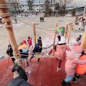 Zahlreiche Kinder klettern auf einem großen Klettergerüst, das auf einem Schulhof steht.