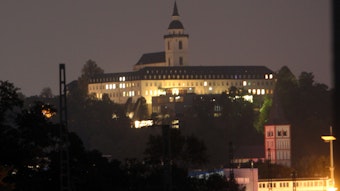 Vor dem nächtlichen Himmel hebt sich die erleuchtete Abtei auf dem Michaelsberg ab, der Turm der Kirche ragt in die Höhe. Weiter unten steht die rot-weiße Servatiuskirche.