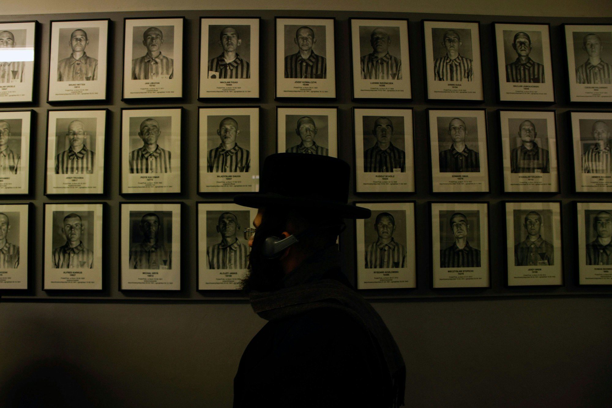 Ein orthodoxer Jude läuft an einer Wand mit Bildern von Auschwitz-Opfern vorbei.