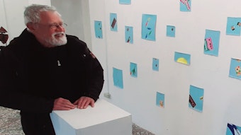Klaus Wolf an eine Pult vor einer Wand mit Bildern.