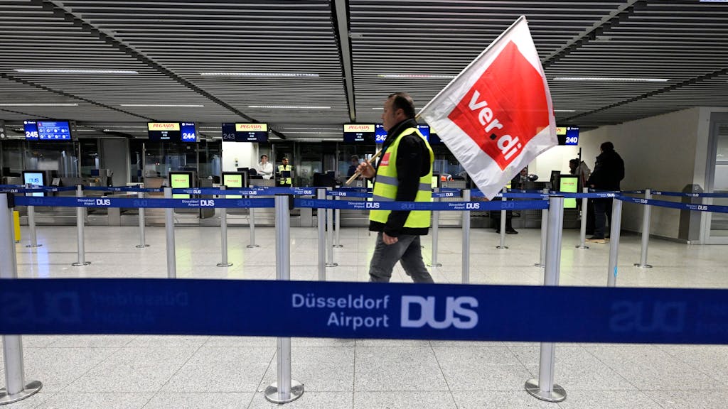 Mann mit Flagge von Verdi spaziert durch den Flughafen in Düsseldorf. Die Gewerkschaft hat zum Streik aufgerufen.