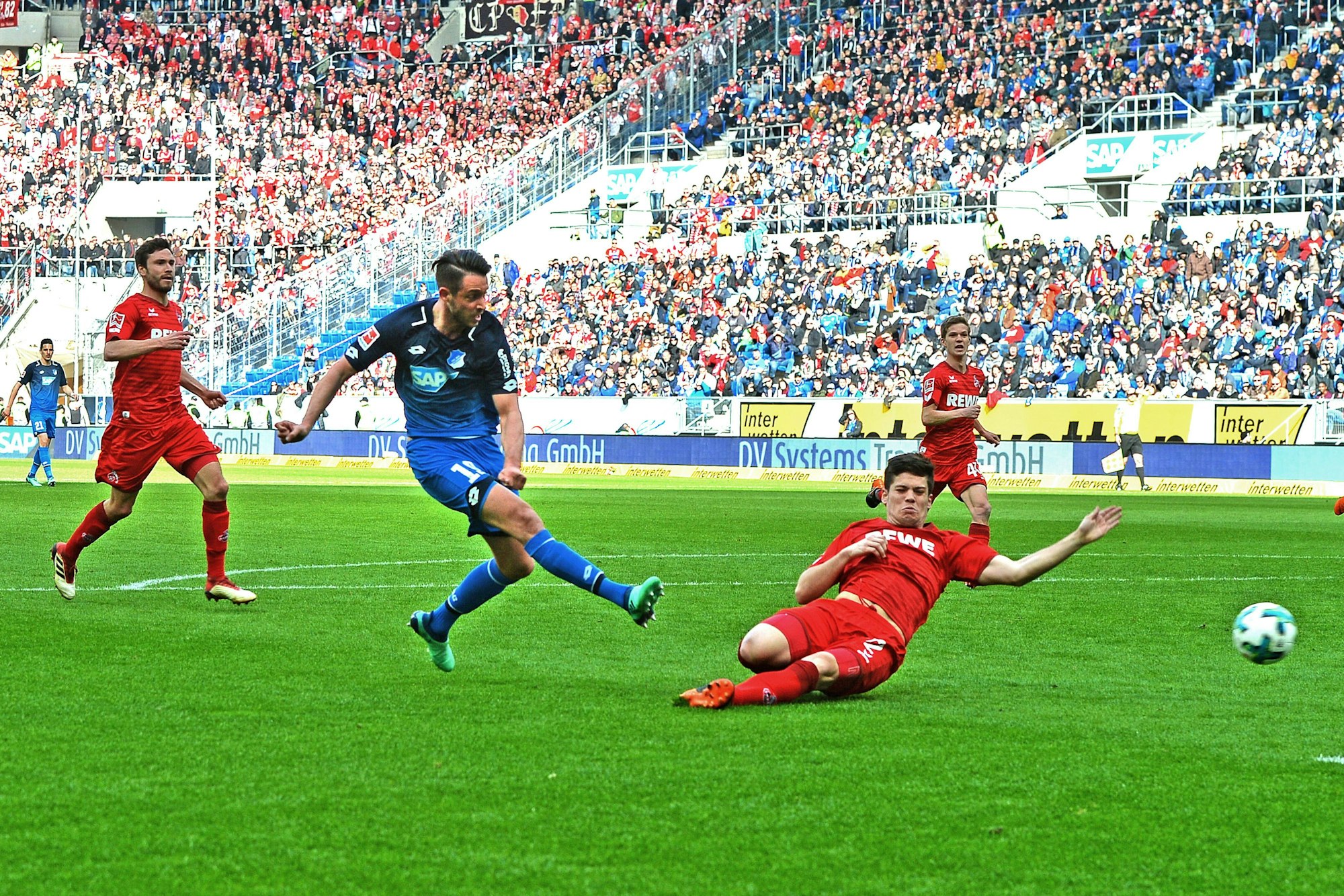 Hoffenheims Mark Uth (M.) schießt den Treffer zum 3:0 gegen den 1. FC Köln, Kölns Jorge Mere versucht es noch vergeblich per Grätsche zu verhindern.