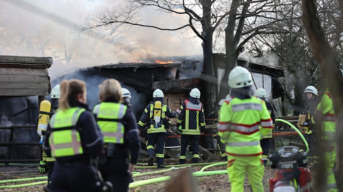 Feuerwehrleute, Sanitäter und Polizeibeamte stehen während eines Brands an einer Scheune im Kölner Stadtteil Rodenkirchen am Samstag, 28. Januar 2023. Bei dem Feuer ist eine Person tot aufgefunden worden.