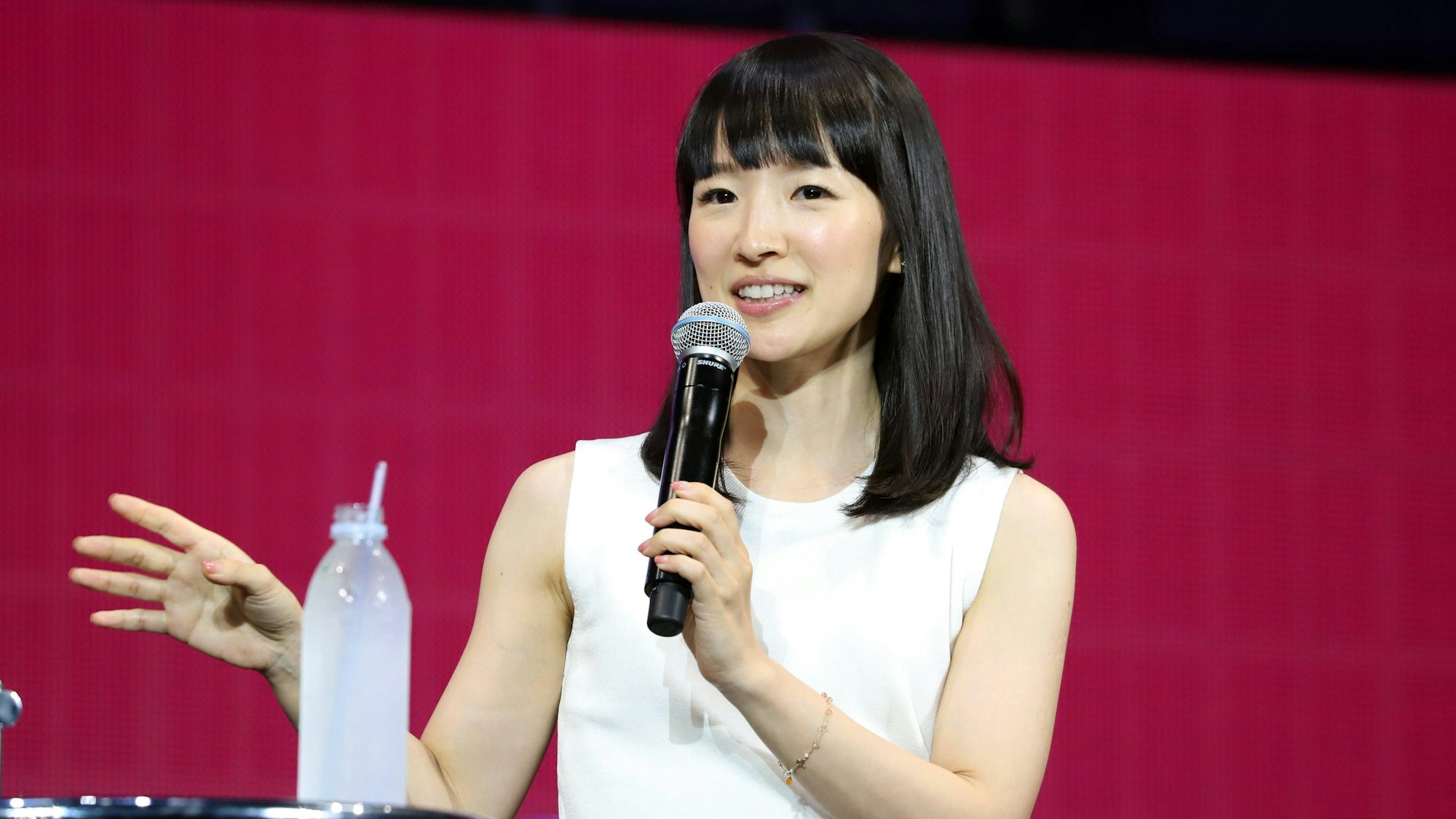 Aufräum-Expertin Marie Kondo 2019 bei einem Vortrag in Japan. Sie trägt ein weißes Oberteil, gestikuliert mit der rechten Hand und hält ein Mikrofon.