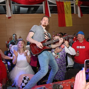 Ein Mann steht bei einer Karnevalssitzung mit einer Gitarre auf einem Tisch.