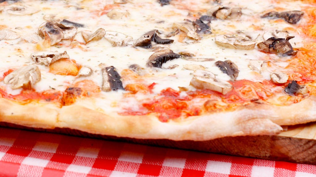 Eine Pizza Funghi (mit Pilzen) liegt auf einem Tisch.