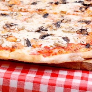 Eine Pizza Funghi (mit Pilzen) liegt auf einem Tisch.