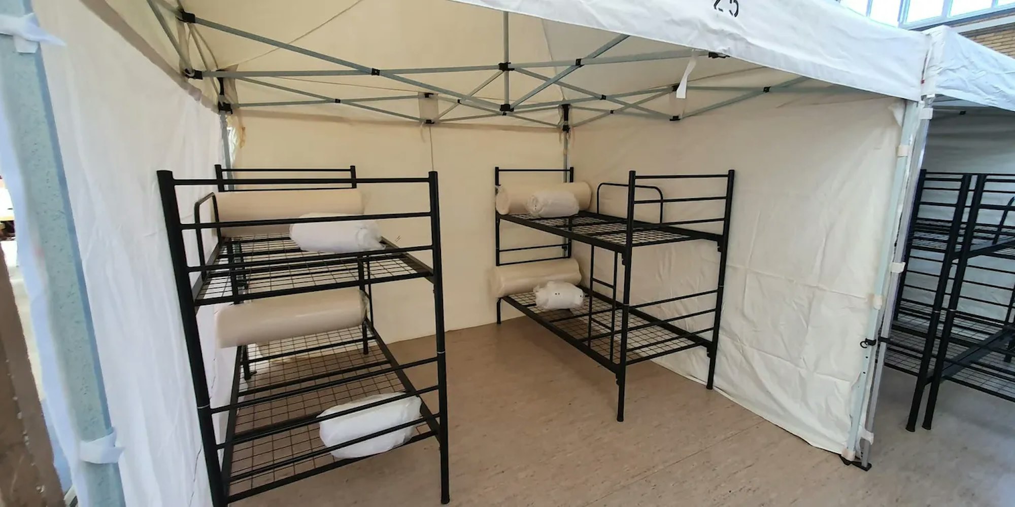 Das Foto zeigt eine Turnhalle in Frechen, in der Geflüchtete wohnen. In Zelten befinden sich jeweils zwei Doppelbetten. 

