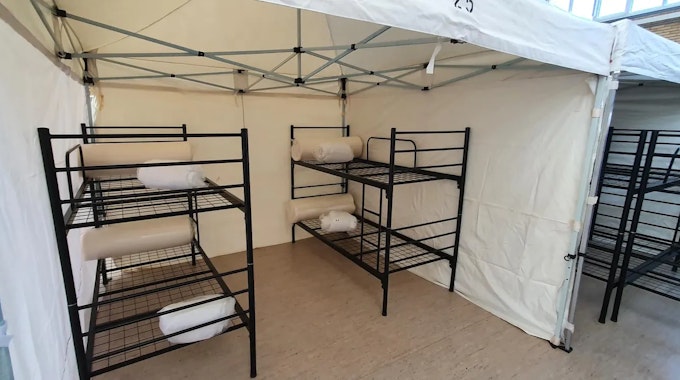 Das Foto zeigt eine Turnhalle in Frechen, in der Geflüchtete wohnen. In Zelten befinden sich jeweils zwei Doppelbetten.