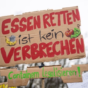 Bei einer Demonstration trägt ein Teilnehmer vor dem Brandenburger Tor ein Plakat mit der Aufschrift „Essen retten ist kein Verbrechen - Containern legalisieren!“.