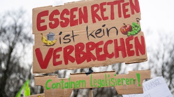 Bei einer Demonstration trägt ein Teilnehmer vor dem Brandenburger Tor ein Plakat mit der Aufschrift „Essen retten ist kein Verbrechen - Containern legalisieren!“.