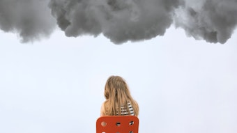 Ein Mädchen sitzt auf einem roten Stuhl unter dunklen Wolken.
