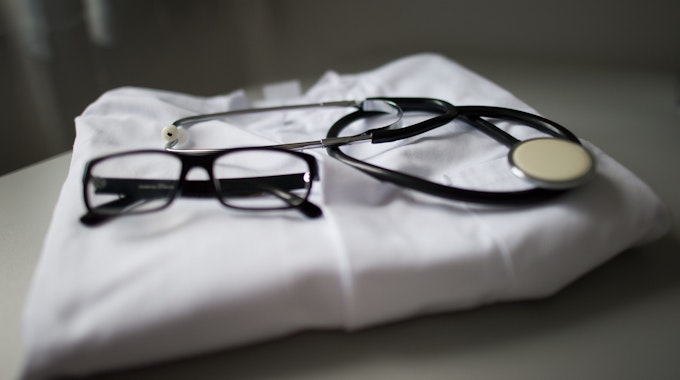 Eine Brille und ein Stethoskop liegen auf einem gefalteten Arztkittel.