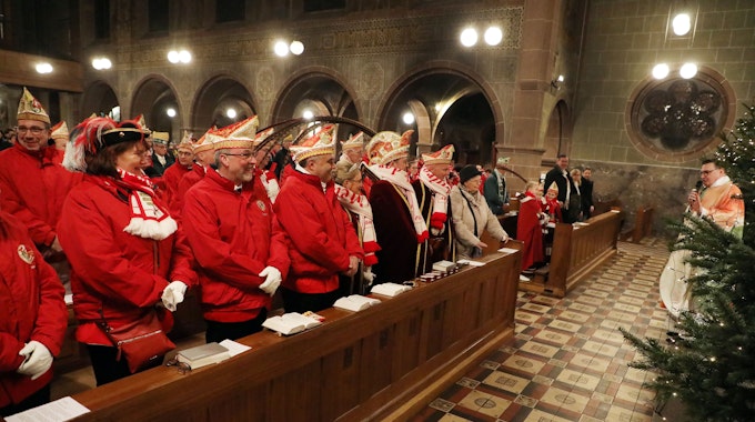 In der Kirche sitzen mit roten Jacken und Narrenkappen bekleidet Bergisch Gladbacher Karnevalisten, vorne redet Kreisdechant Norbert Hörter.