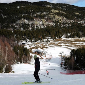 Es ist ein Skifahrer zu sehen, der auf der Piste steht und bergab schaut.