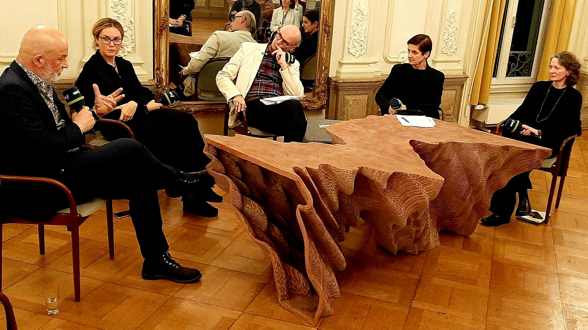 Fünf Personen diskutieren vor Publikum um einen Tisch sitzend.