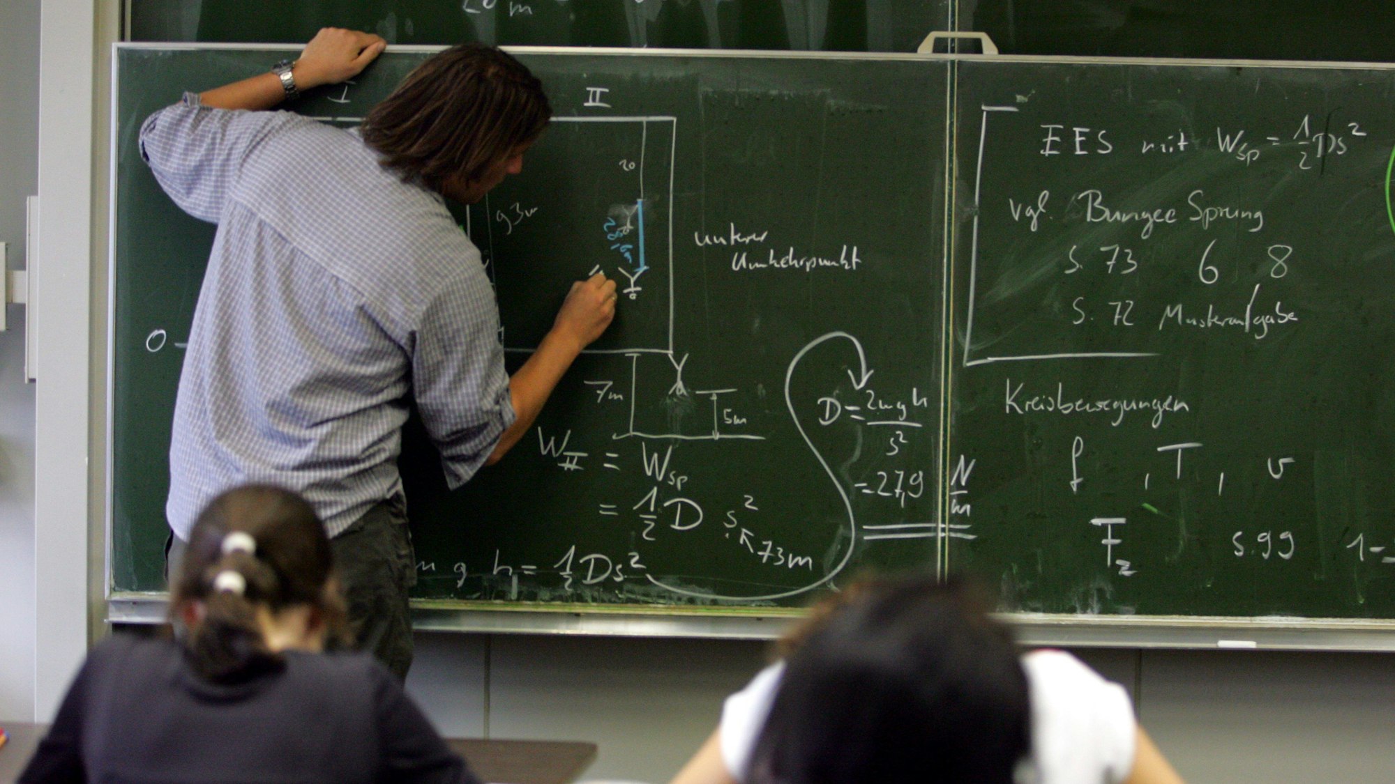 Ein Lehrer schreibt Physik-Formeln an die Tafel.