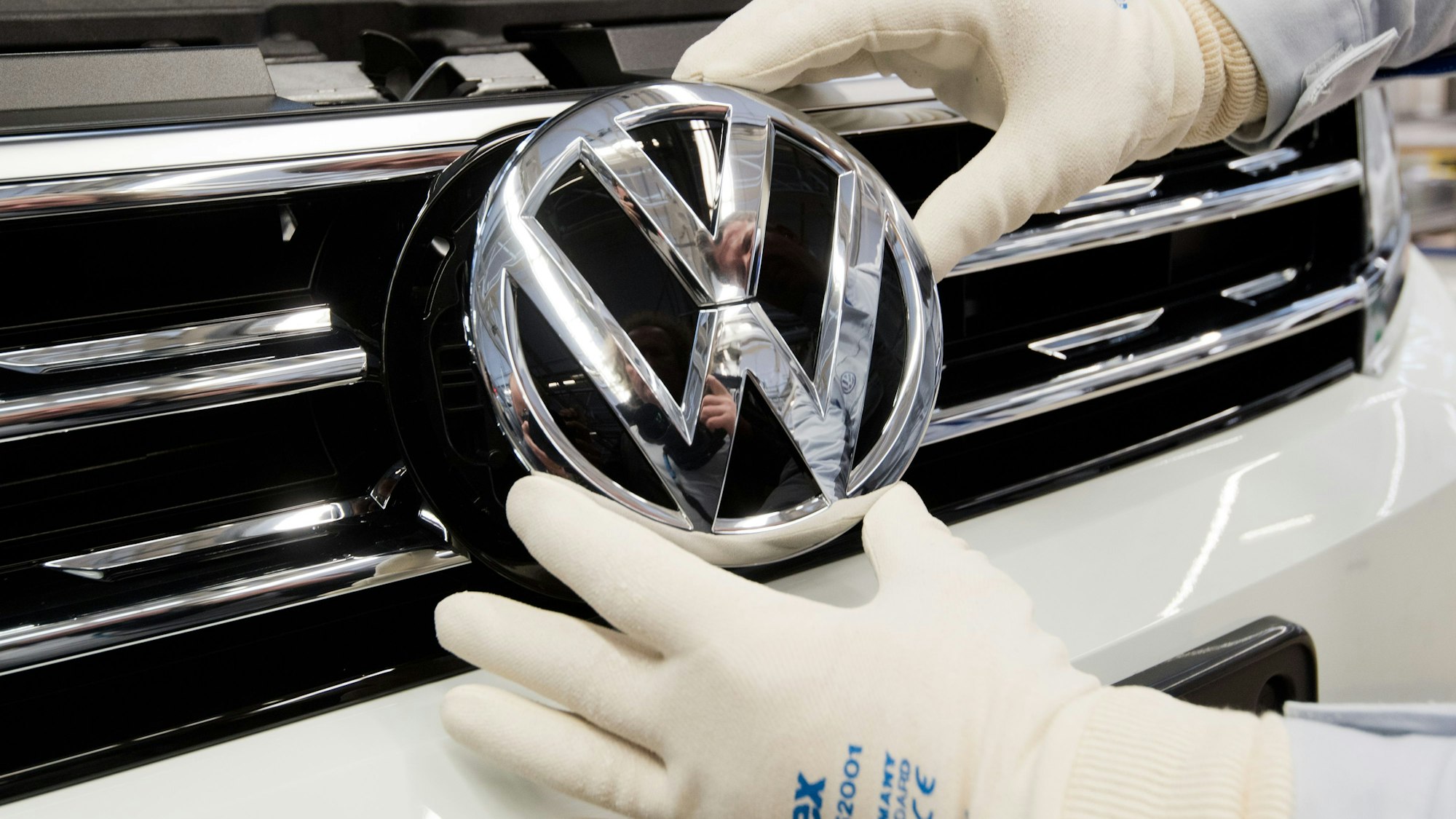 Ein Mitarbeiter montiert ein VW Logo an die Front eines VW Tiguan in der Endmontage im VW Werk.
