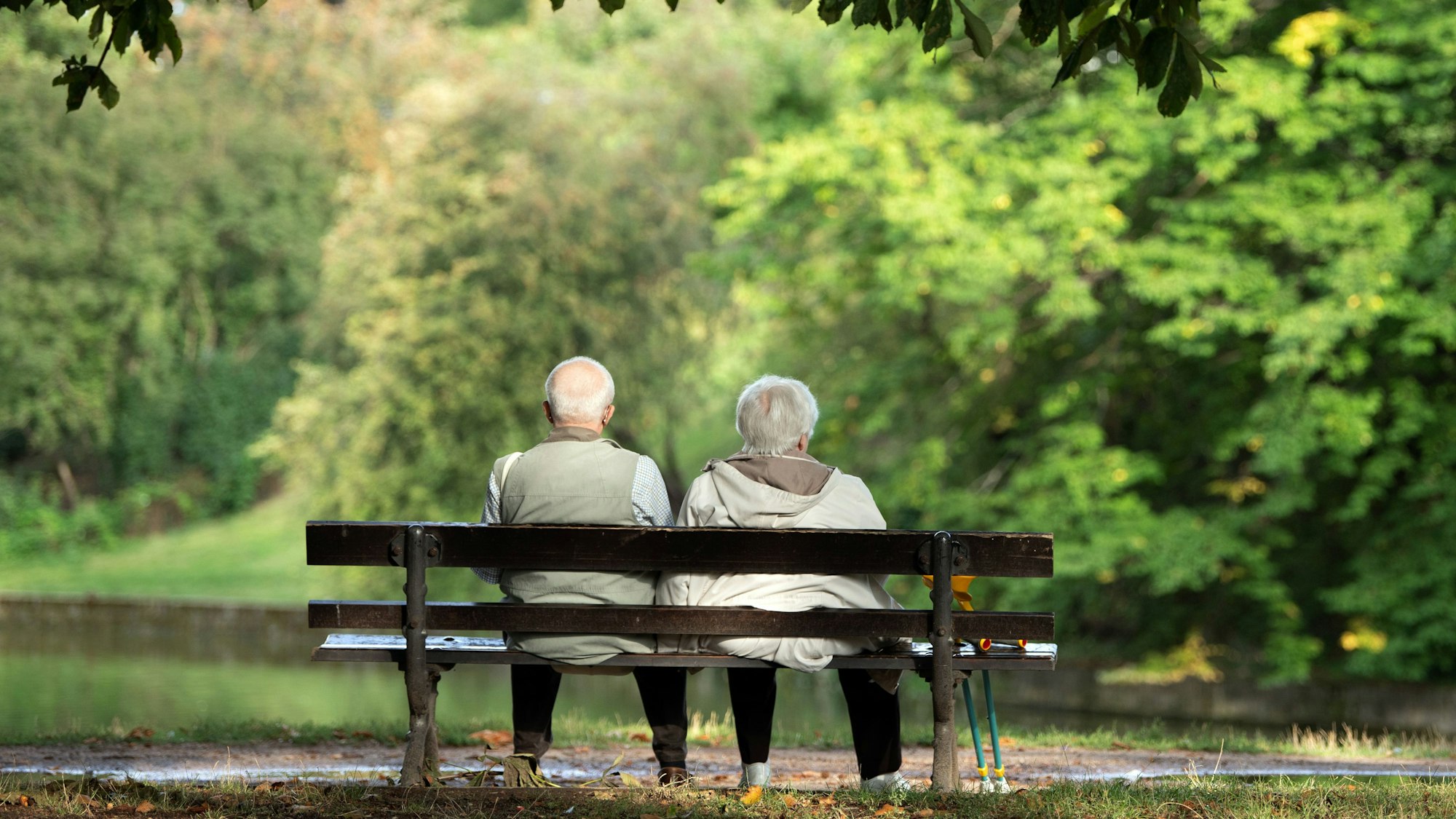Ein Rentner und eine Rentnerin sitzen auf einer Bank im Park. Bei der Aufnahme handelt es sich um ein Symbolfoto.