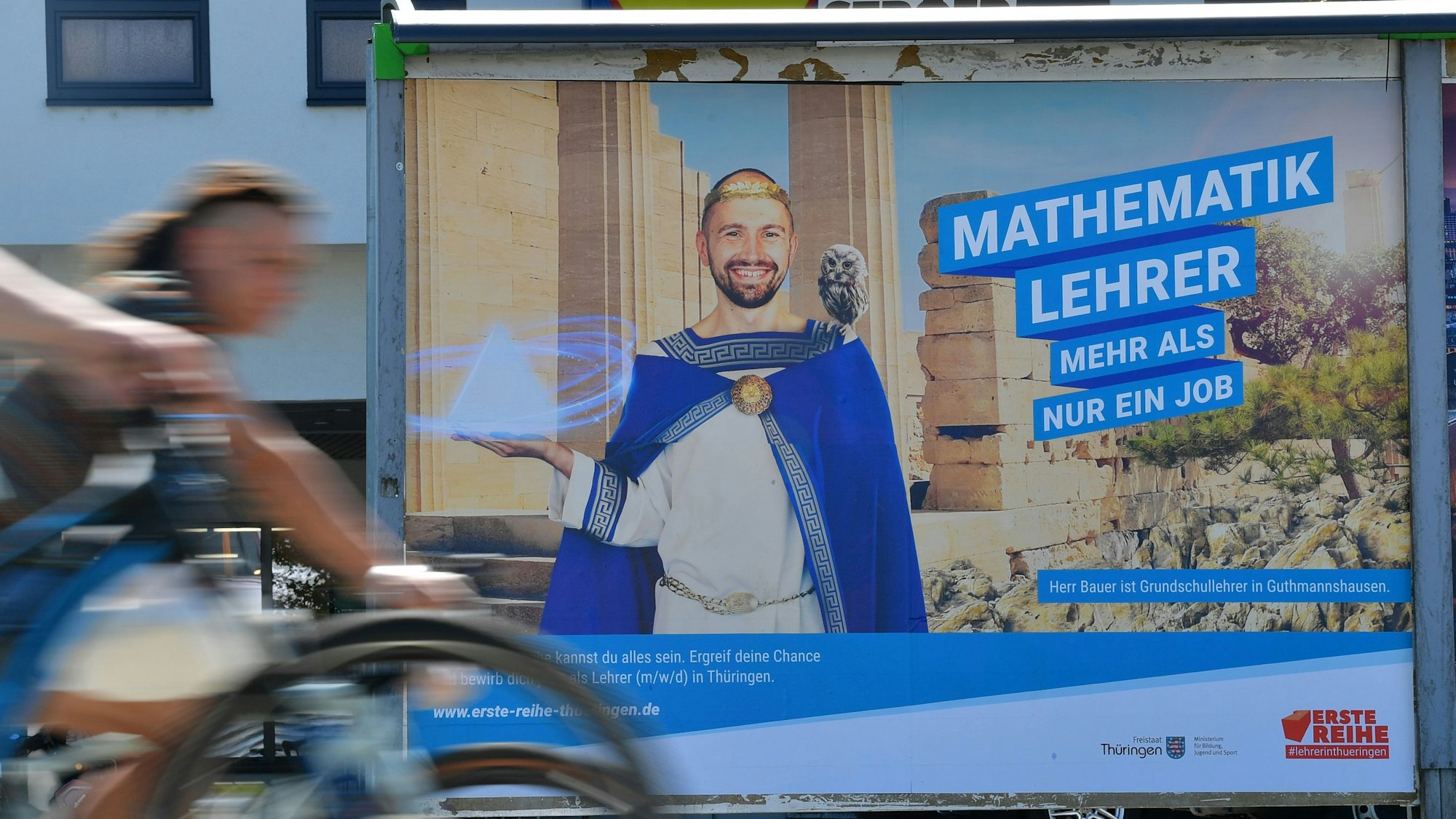 Radler fahren an einem Plakat vorbei, auf dem der Freistaat Thüringen um Quereinsteiger als Mathematiklehrer wirbt. Der Werbeslogan lautet: „Mathematiklehrer – Mehr als nur ein Job“