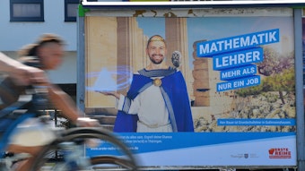 Radler fahren an einem Plakat vorbei, auf dem der Freistaat Thüringen um Quereinsteiger als Mathematiklehrer wirbt. Der Werbeslogan lautet: „Mathematiklehrer – Mehr als nur ein Job“