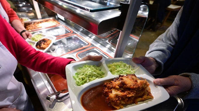 Das Foto zeigt eine Frau, die einen Teller mit Mittagessen verteilt.