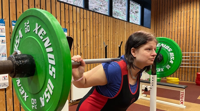 Behinderte Kraftsportlerin Jessica Steinbrück drückt eine Langhantel mit grünen Gewichten in die Höhe.