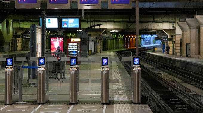 Verlassene Bahnsteige am Bahnhof Montparnasse in Paris. Zu sehen sind mehrere Ticketkontrollsysteme und Bildschirme, die ein rotes Kreuz zeigen.