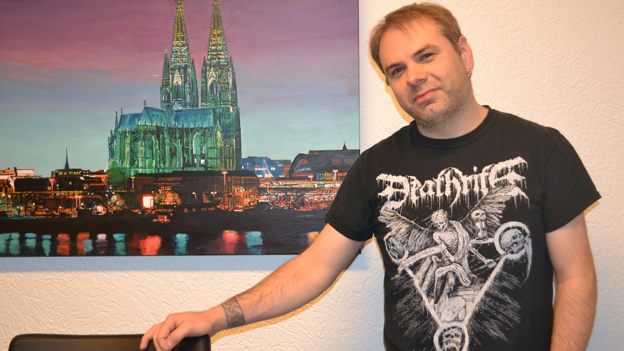 Gerald Bauer, Heavy-Metal-Blogger, vor einem Poster mit dem Kölner Dom.