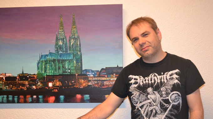 Gerald Bauer, Heavy-Metal-Blogger, vor einem Poster mit dem Kölner Dom.