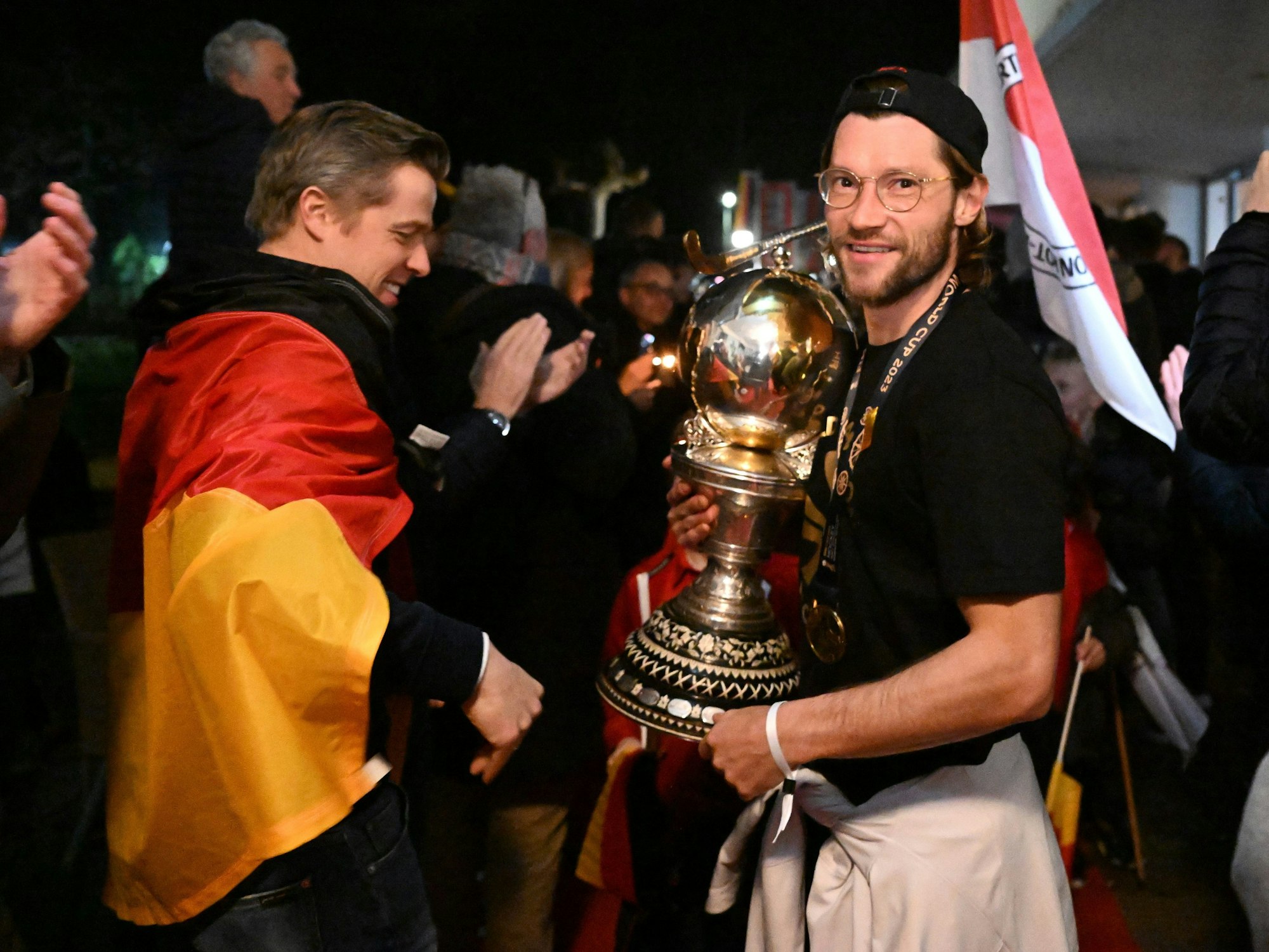 Martin Zwicker (r) hält den Weltmeister-Pokal, ein Mann vor ihm trägt eine Deutschland-Fahne.