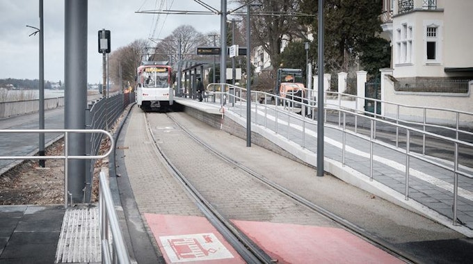 Eine rot-weiße Stadtbahn der Linie 66 steht am neuen Mittelbahnsteig Clemens-August-Straße in der Altstadt von Königswinter. Die Haltestelle hat einen Unterstand aus Glas und Stahl.