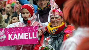 08.02.2016: Rosenmontag in Köln: Jecke stehen verkleidet am Straßenrand und schauen auf den Rosenmontagszug. Ein Kind hält ein Schild, auf dem „Kamelle“ steht.