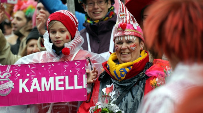 08.02.2016: Rosenmontag in Köln: Jecke stehen verkleidet am Straßenrand und schauen auf den Rosenmontagszug. Ein Kind hält ein Schild, auf dem „Kamelle“ steht.