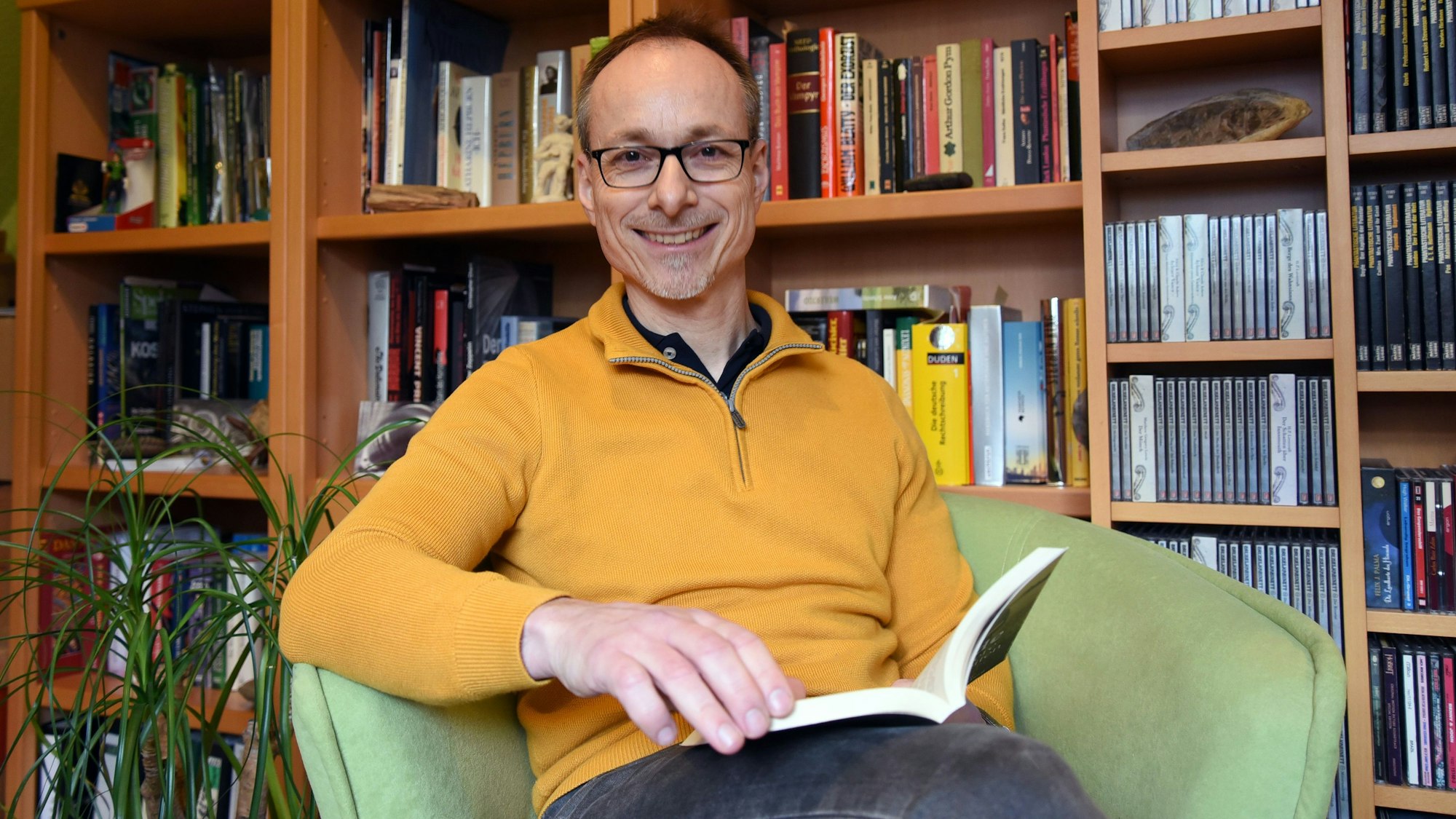 Der Autor Andreas Wöhl sitzt mit einem Buch in einem Sessel.