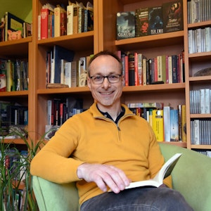 Der Autor Andreas Wöhl sitzt mit einem Buch in einem Sessel.