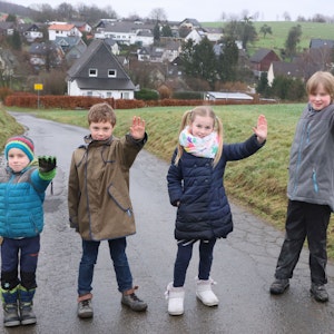 Man sieht die Kinder, wie sie nebeneinander auf dem Feldweg stehen, sie strecken jeweils ihre linke Hand als Stop-Signal nach vorne.