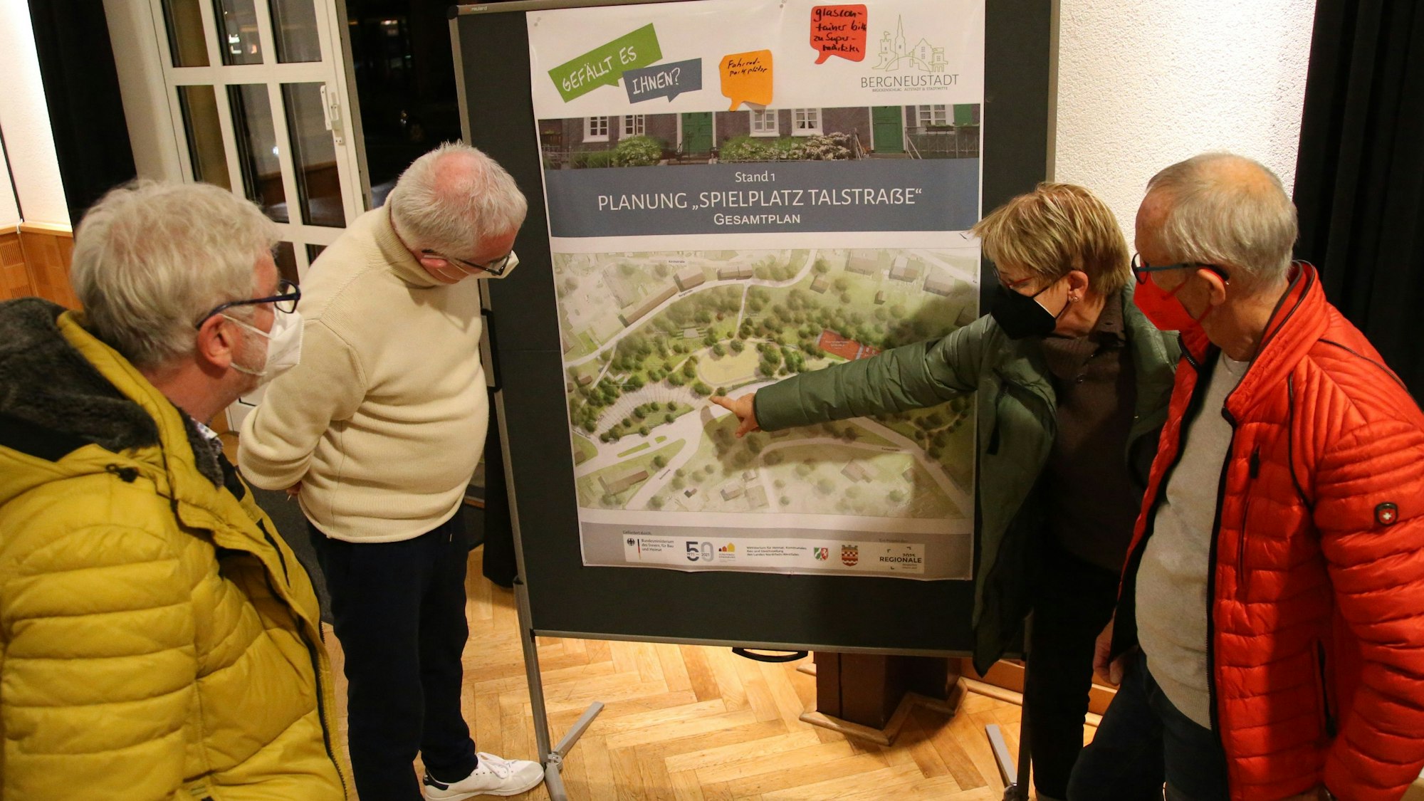 Zu sehen sind vier Menschen, die auf die großformatige Karte eines Spielplatzes schauen und über die Details sprechen.