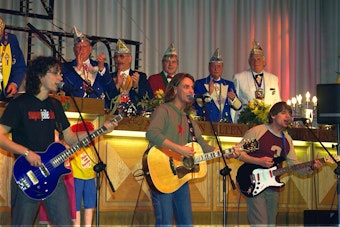 Die Band Brings spielt in einer Reihe auf der Bühne. Im Hintergrund der Elferrat.