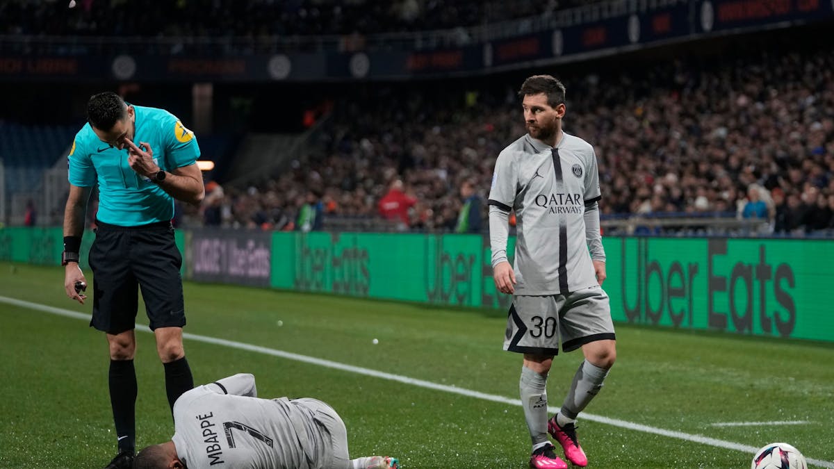 Kylian Mbappé krümmt sich im Spiel von Paris Saint-Germain bei HSC Montpellier am Boden. Lionel Messi und der Schiedsrichter stehen neben ihm.