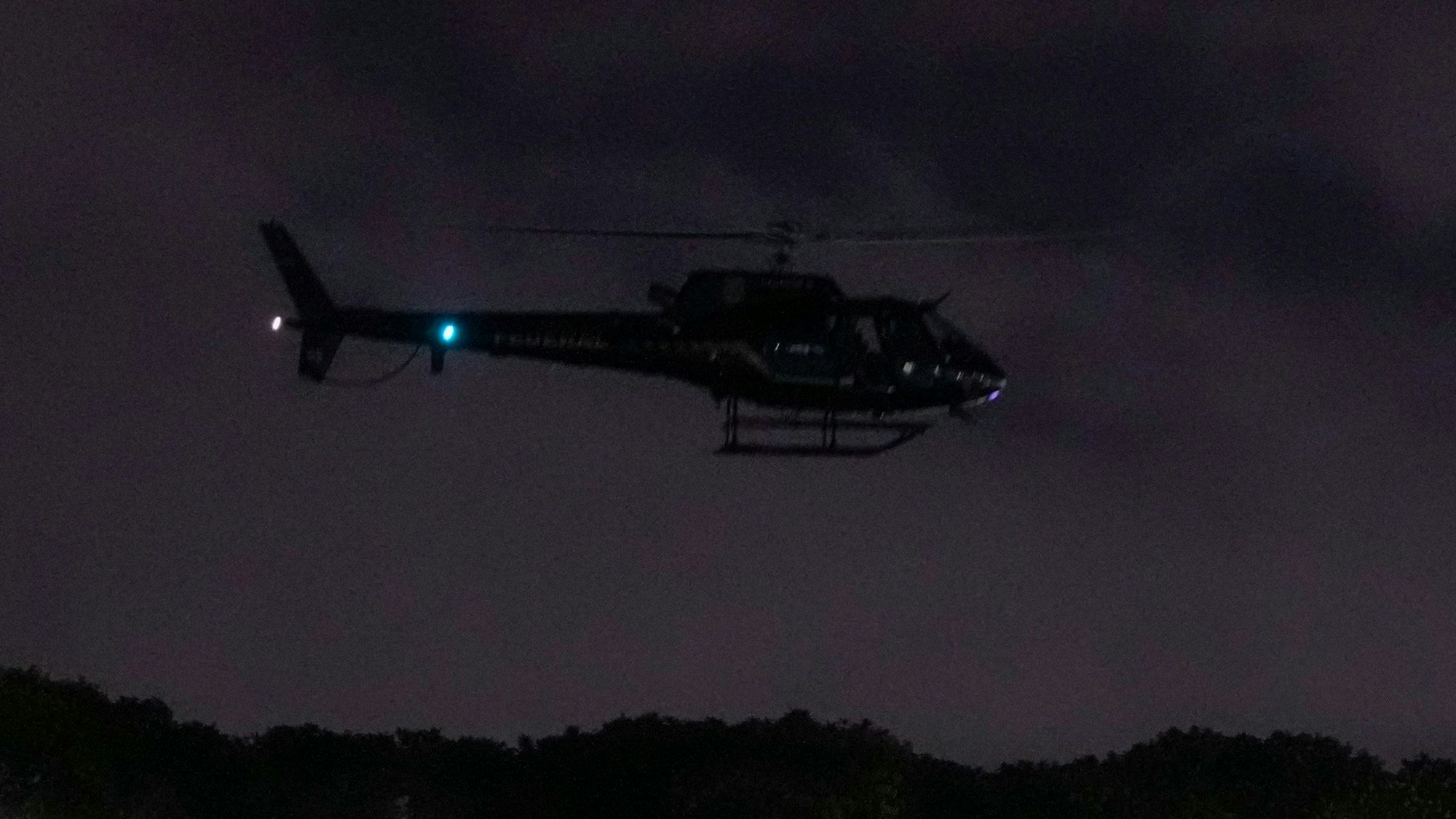 Ein Polizeihubschrauber fliegt in der Nacht über eine hügelige Landschaft.