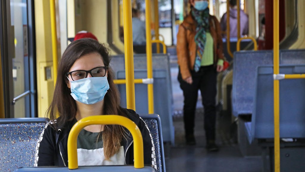 Eine Frau sitzt mit einer Schutzmaske in einer Straßenbahn.&nbsp;