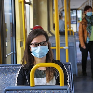 Eine Frau sitzt mit einer Schutzmaske in einer Straßenbahn.