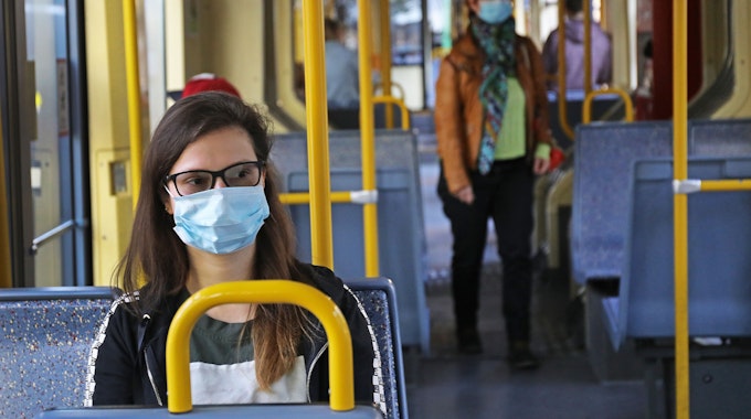 Eine Frau sitzt mit einer Schutzmaske in einer Straßenbahn.