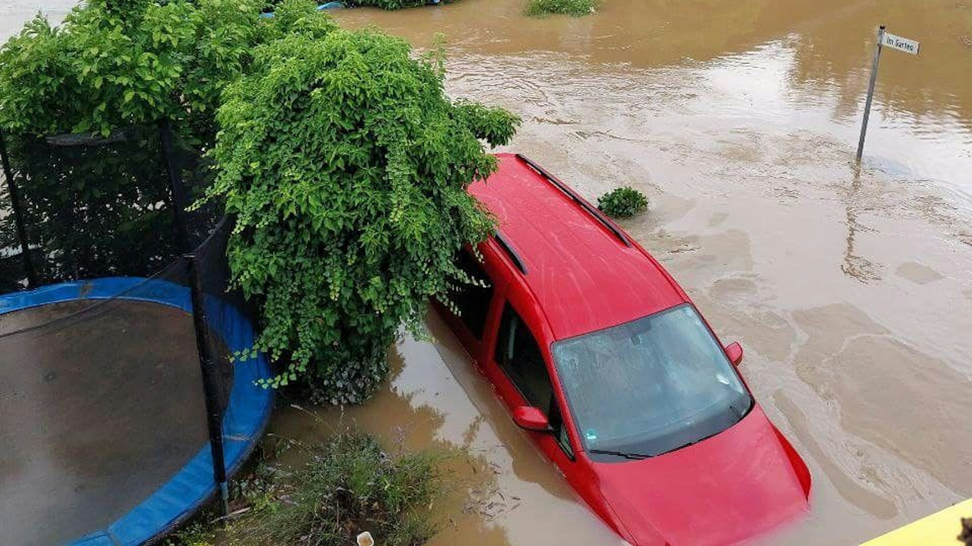Ein rotes Auto steht bis über den Reifen unter Wasser. Auch die Bäume, die daneben stehen, sind überflutet.