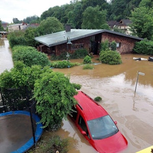 Ein rotes Auto steht bis über den Reifen unter Wasser. Auch die Bäume, die daneben stehen, sind überflutet.