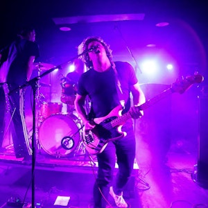 Bassist Julian Knoth von der deutschen Noiserock-Band Die Nerven brüllt ins Mikrofon. Gitarrist Max Rieger steht im Kölner Luxor auf dem Schlagzeug-Podest von Drummer Kevin Kuhn.