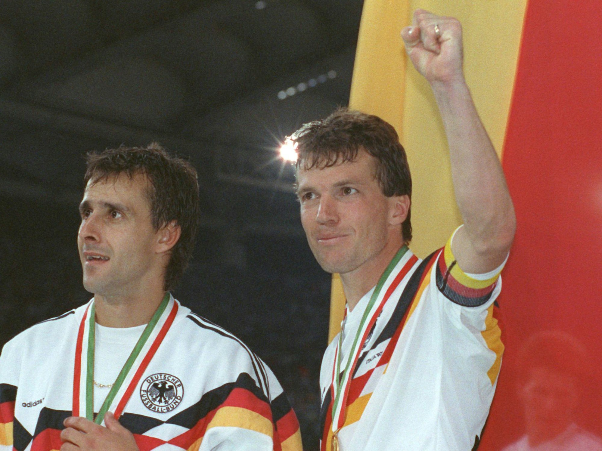 Der deutsche Mittelfeldspieler und Kapitän Lothar Matthäus (r.) und sein Mitstreiter Pierre Littbarski (l.) bejubeln vor der deutschen Fahne den WM-Titel in Italien.