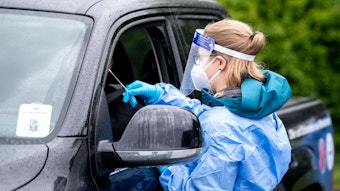 Eine Mitarbeiterin eines Corona-Testzentrums trägt Schutzkleidung und führt bei einem Autofahrer einen Test durch.