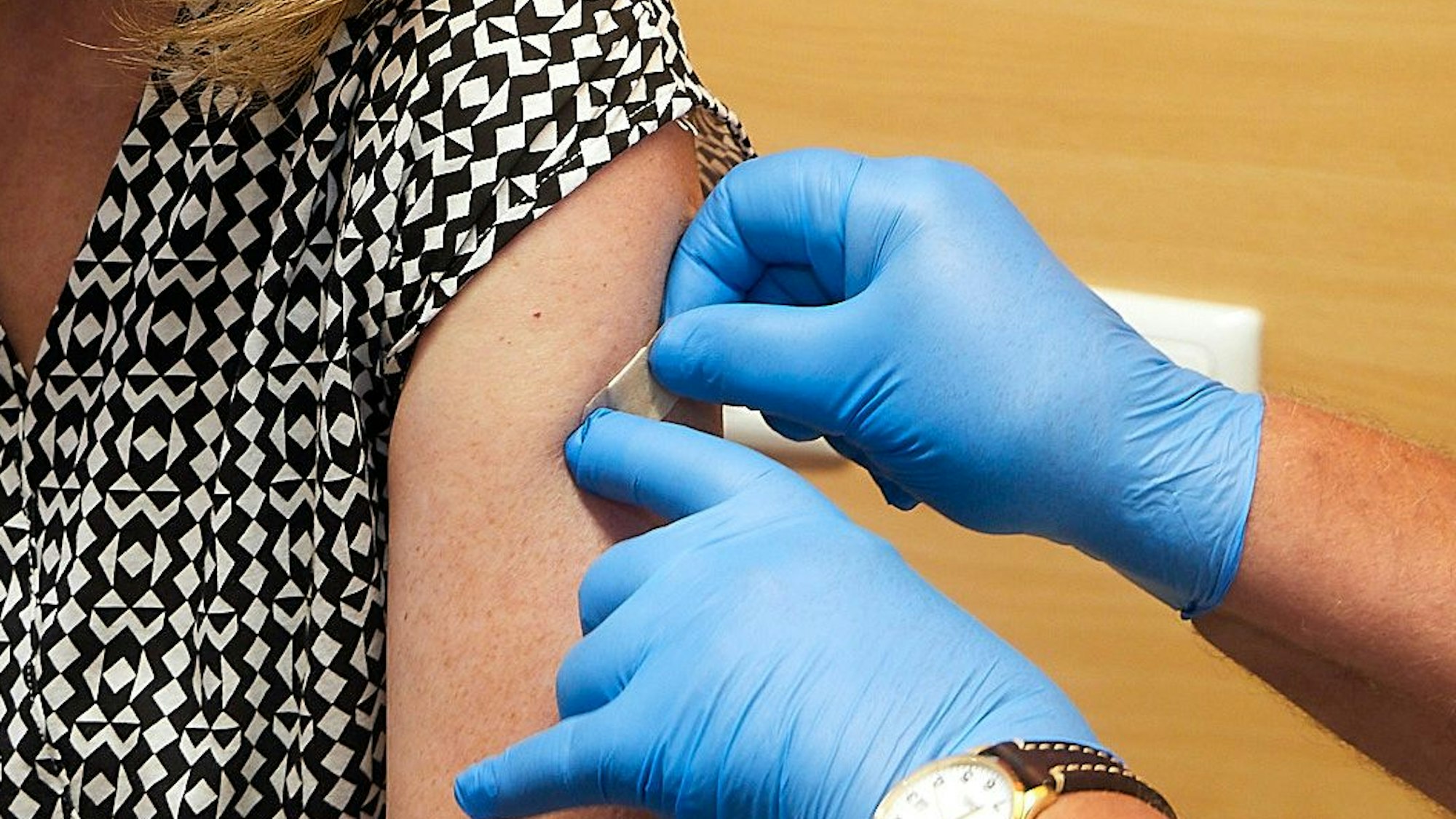 Nach einer Corona-Impfung klebt ein Arzt ein Pflaster auf den Arm einer Frau.